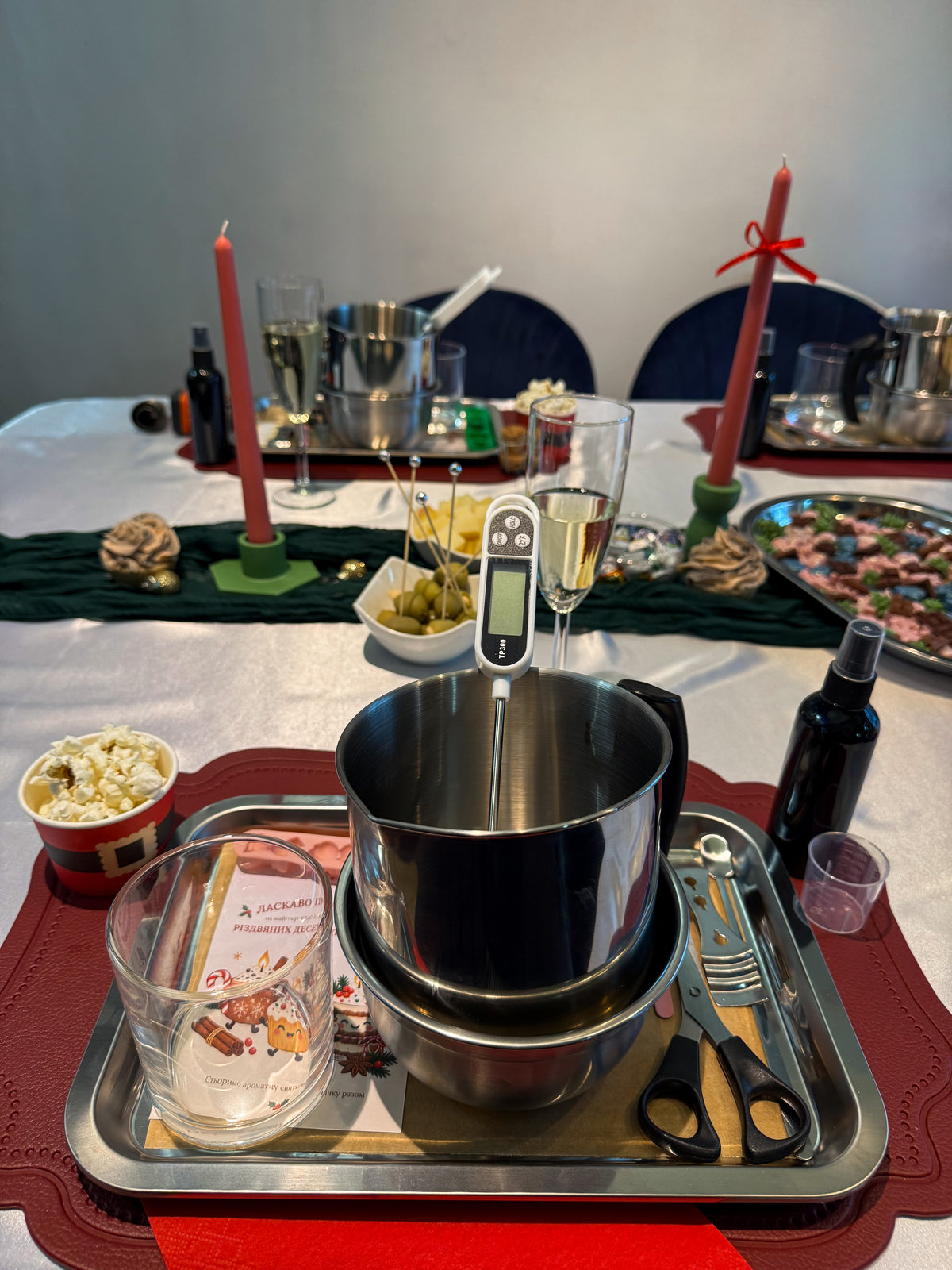 Candle-making workstation prepared for a Christmas dessert candle workshop in Vienna, featuring a wax melting pot, digital thermometer, glass candle container, tools and festive table decorations.
