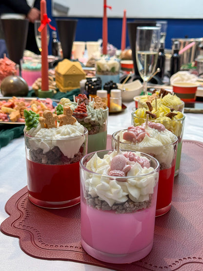 Handmade Christmas dessert candles in pink, red and green, decorated with whipped wax, gingerbread figures, Christmas trees and festive decorations at a candle-making workshop in Vienna.