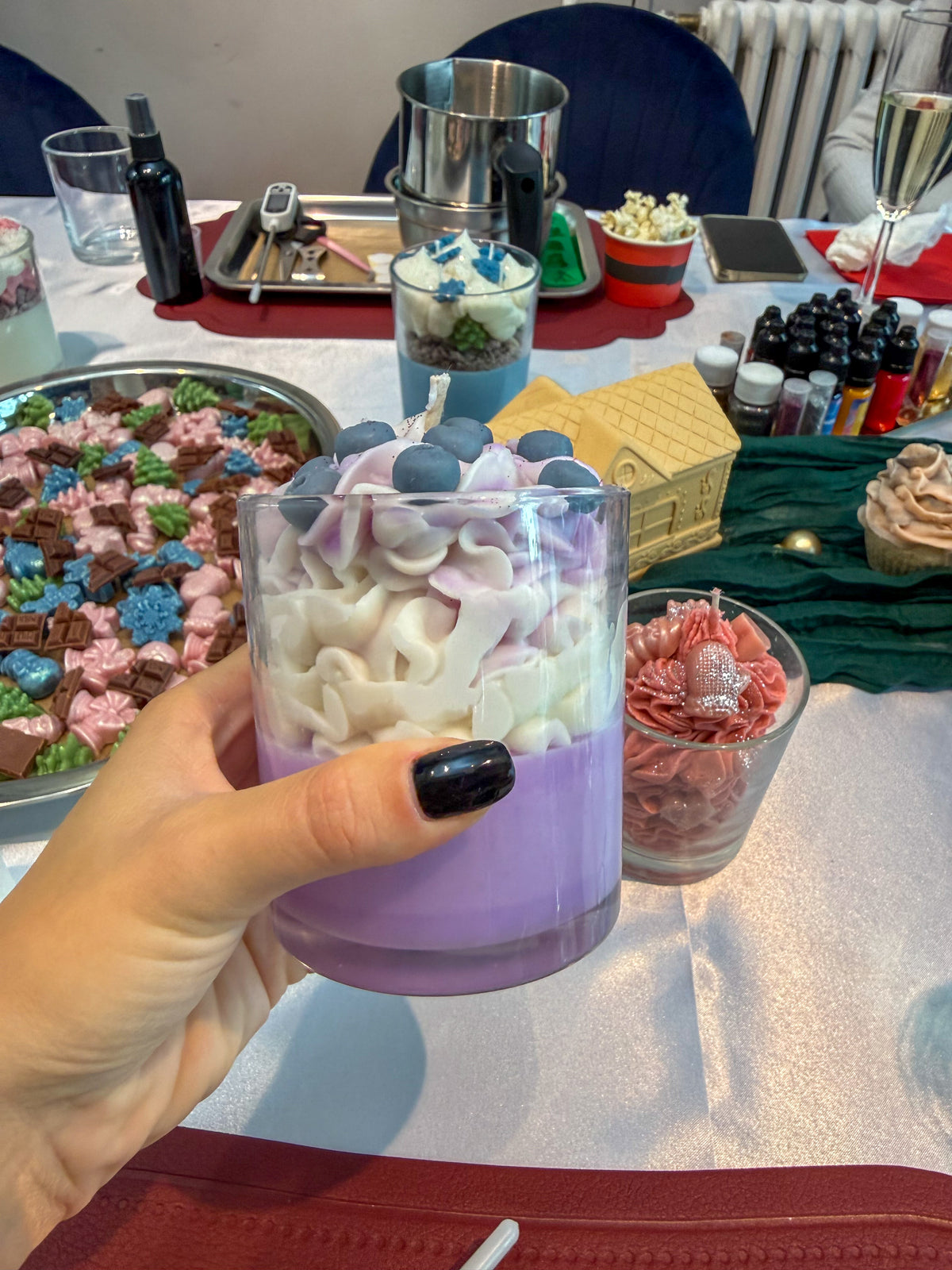 Hand holding a handmade purple Christmas dessert candle in a glass, decorated with whipped wax and festive toppings at a candle-making workshop in Vienna.